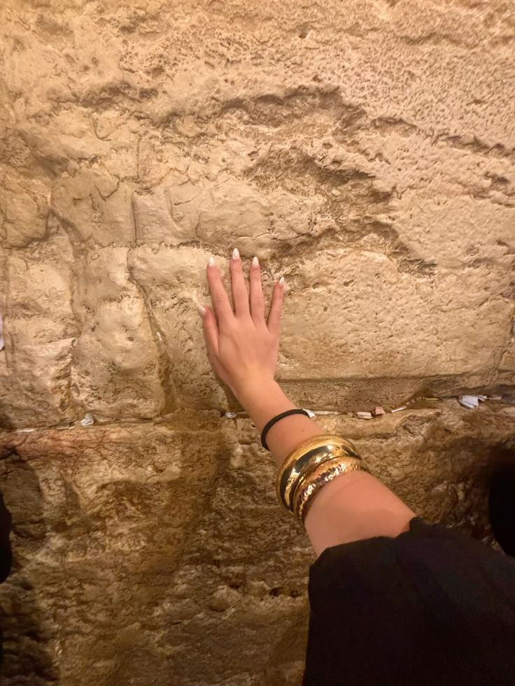Hand with gold bangles resting on the Western Wall, prayer notes tucked into the stones